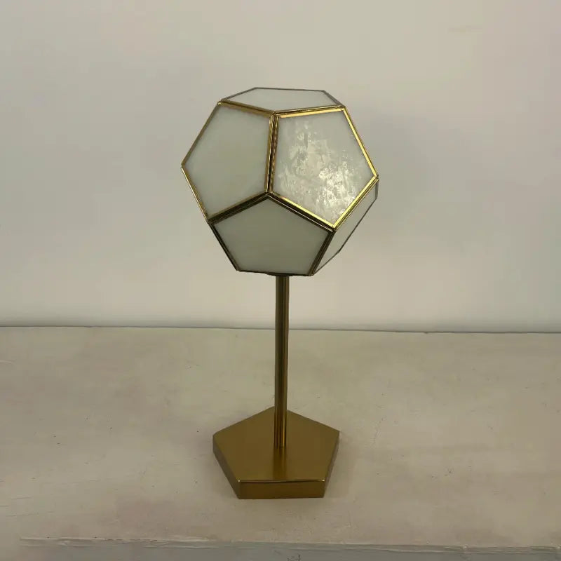 Geometric table lamp with gold base and white glass shade on a plain background