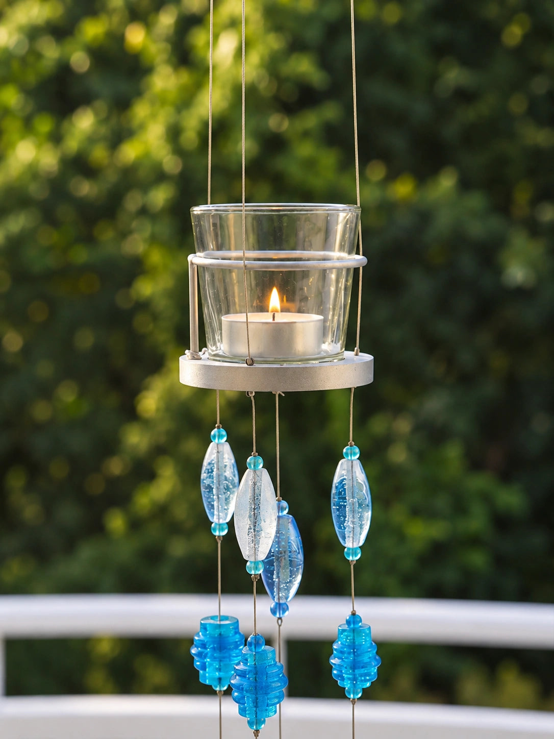 Blue Glass Beaded Hanging Votive – ILLUMEA handcrafted decorative candle holder featuring a clear glass votive, silver metal frame and cascading strands of blue and turquoise glass beads