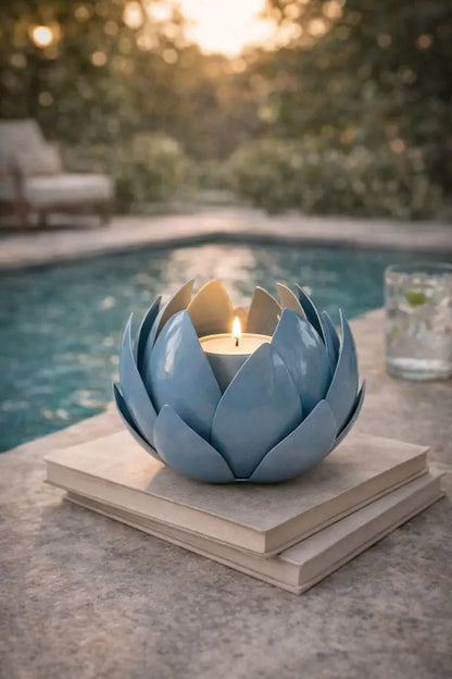 Blue ceramic lotus flower candle holder with a lit candle on a stone surface by a pool.