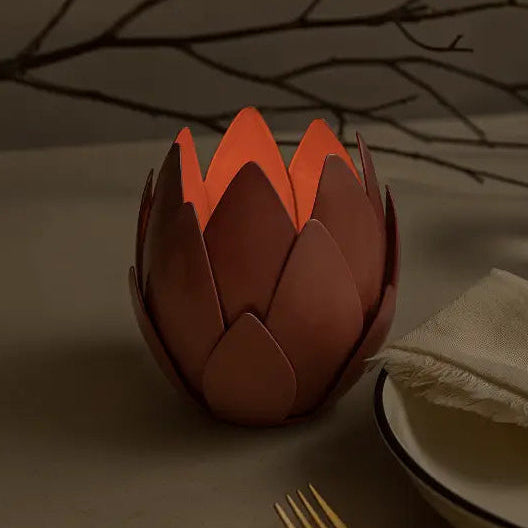 Decorative artichoke-shaped candle holder on a table setting with a glass of water and a gold napkin ring.