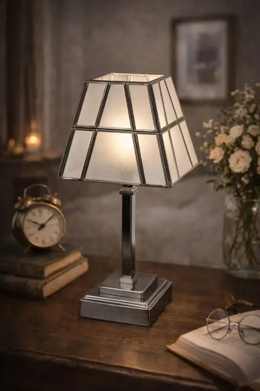 Table lamp with stained glass shade on a wooden surface, surrounded by books and a clock.