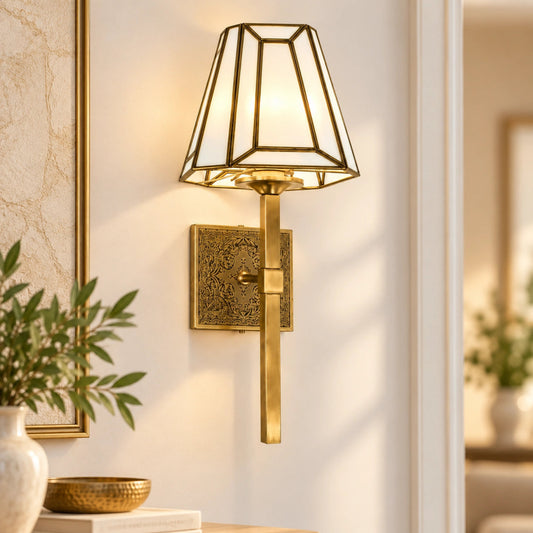 Antique Brass Geometric Wall Sconce by ILLUMEA featuring a tapered glass shade with elegant geometric brass framing and warm ambient illumination