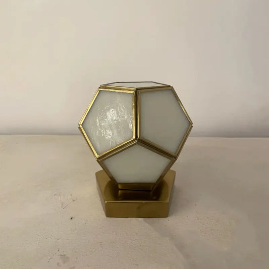 Geometric lamp with gold frame and white glass on a beige surface