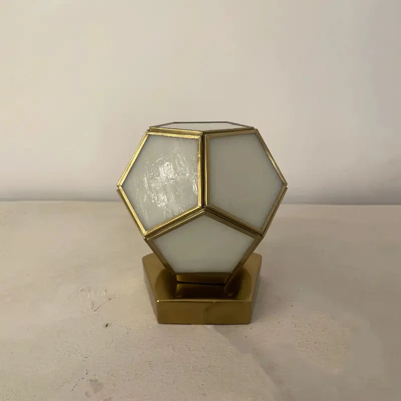 Geometric lamp with gold frame and white glass on a beige surface