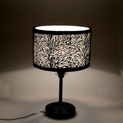 Black table lamp with a decorative white patterned shade on a dark background