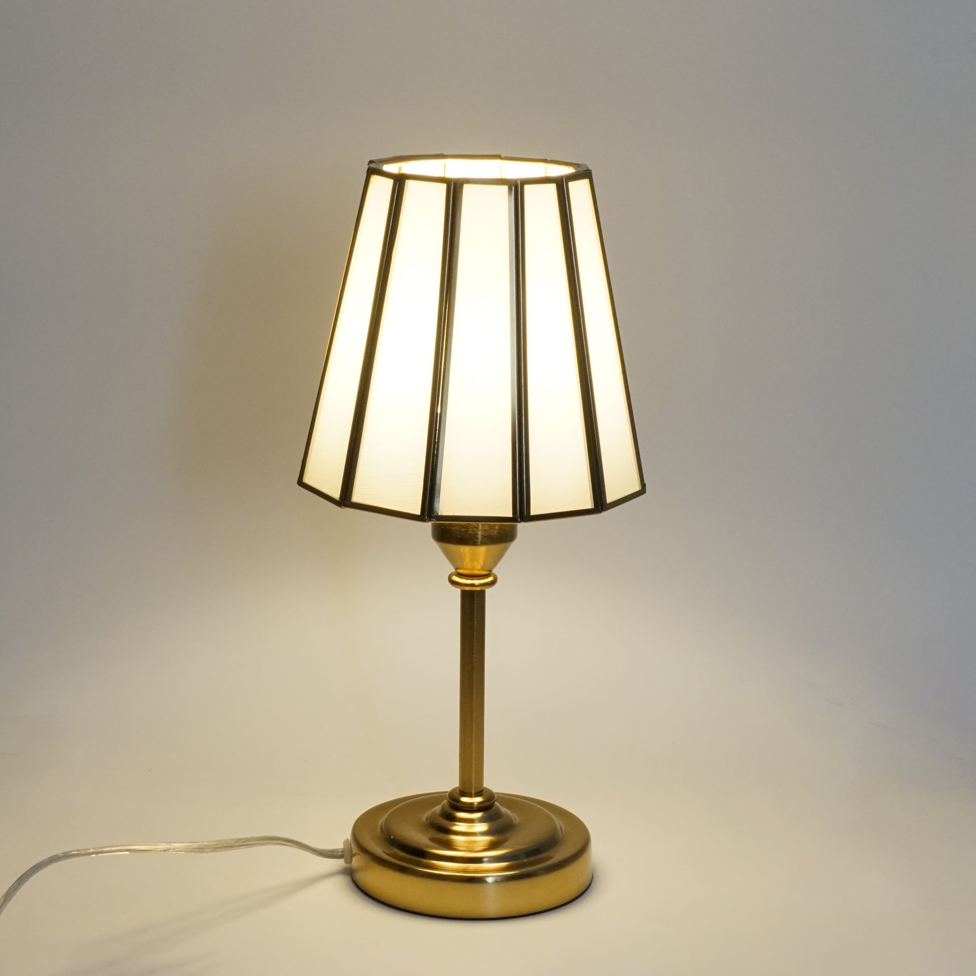 Table lamp with a white shade and gold base on a neutral background