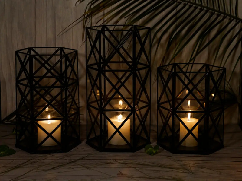 Three black geometric candle holders with lit candles on a wooden surface.